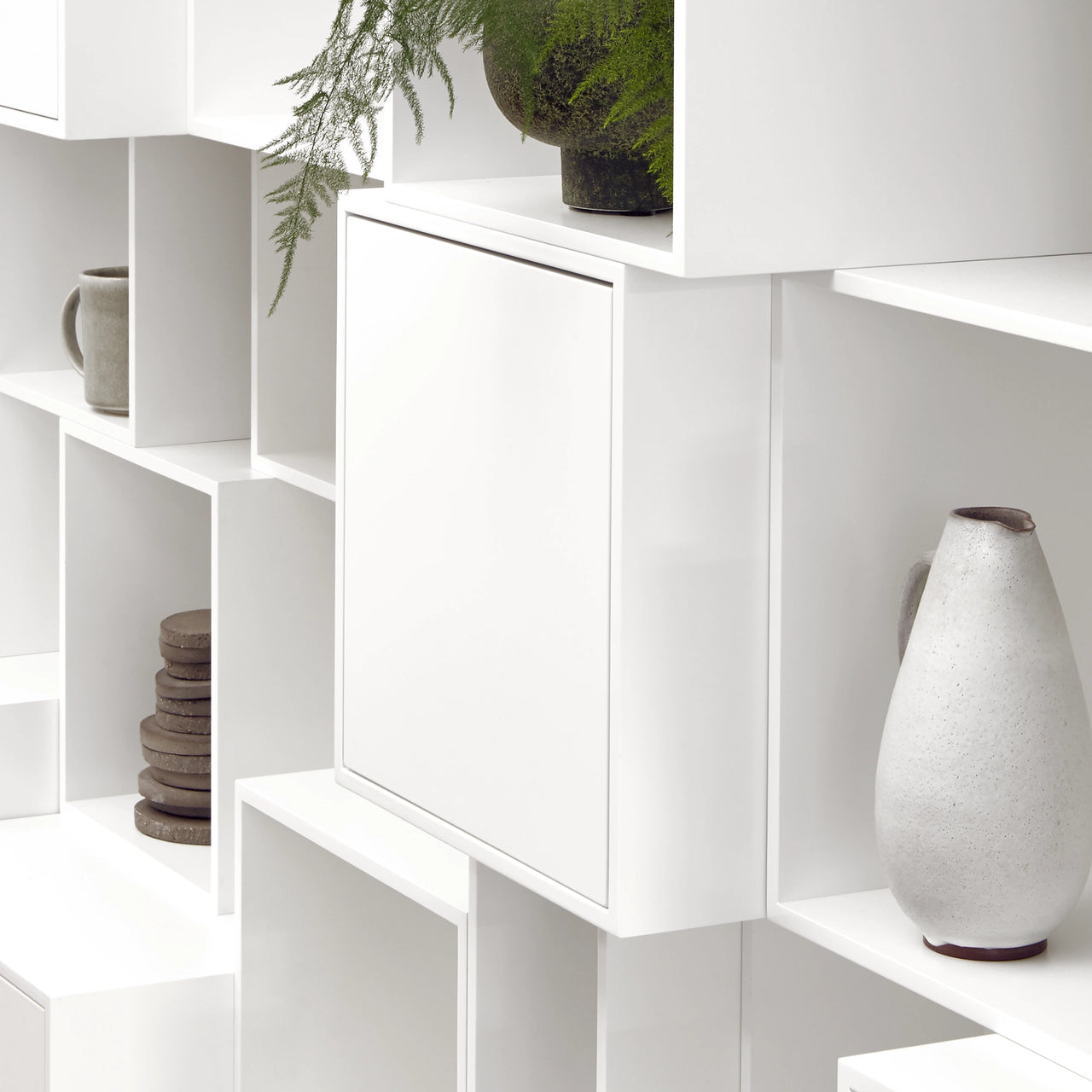 Modernes weißes Regal mit seidenmatten Oberflächen, dekoriert mit Keramikobjekten, Holzuntersetzern und einer Pflanze – minimalistisches, funktionales Design