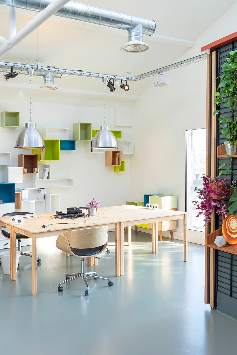 Moderner Showroom mit Cubit Regalsystem in verschiedenen Farben an der Wand, schlichten Holztischen und Pflanzen in industriell inspirierter Umgebung