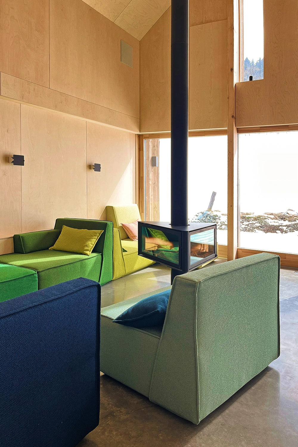 Innenaufnahme eines hellen Showrooms mit Kamin und modularen Cubit Sofas in verschiedenen Grüntönen