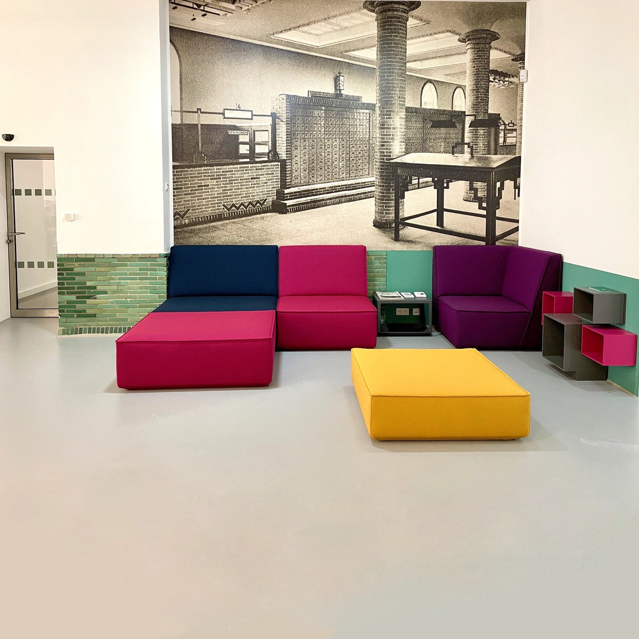 Modular Cubit sofas in bold colors such as magenta, blue and yellow in the foyer of the Kunstmuseum Mülheim in front of a historical wall graphic
