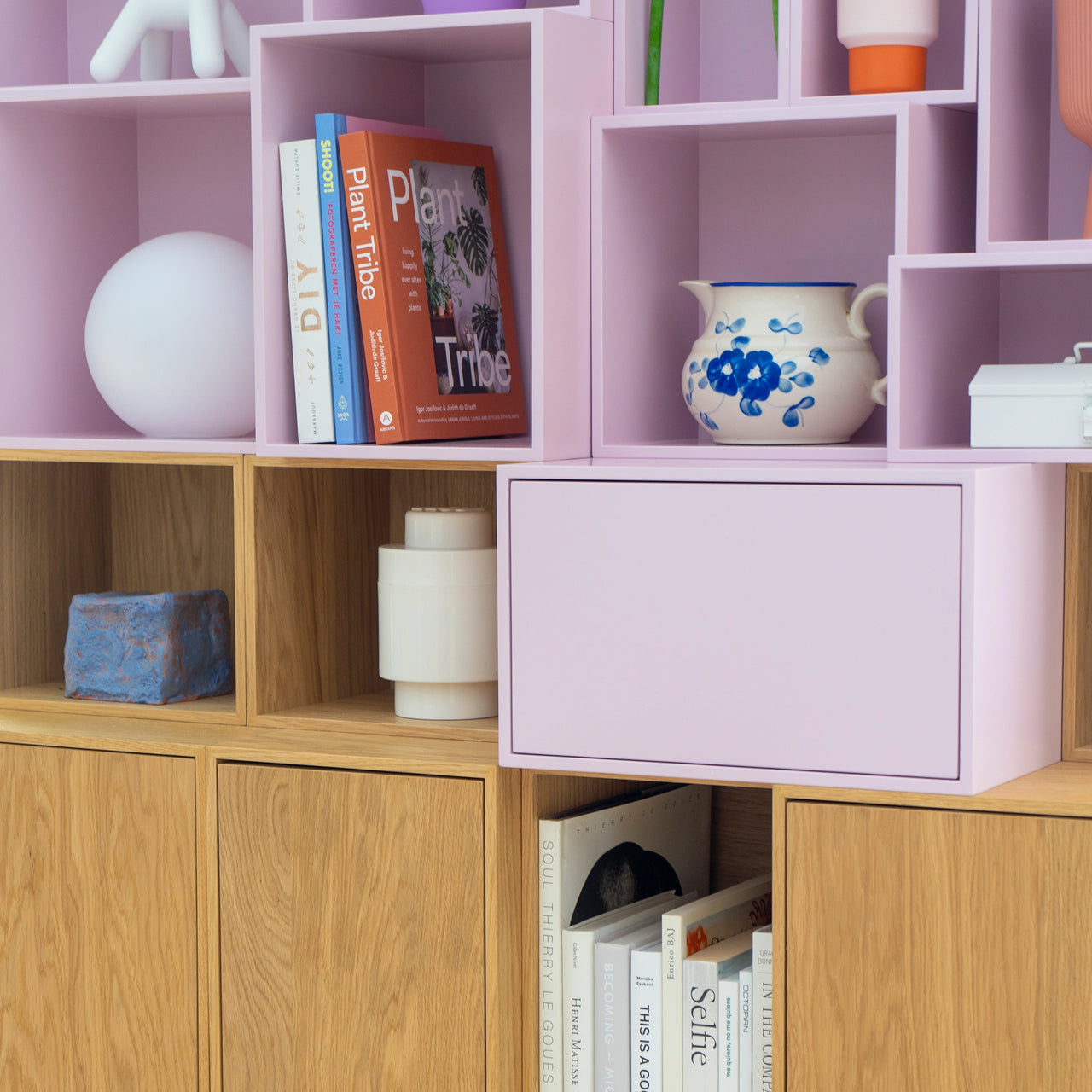Detailed view of a modular shelf with pastel pink and wooden modules, filled with books and decorative objects