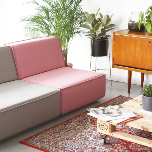 2 Sitzer Sofa in Grau und Rosa, kombiniert mit Holzmöbeln und Pflanzen in einem gemütlichen Wohnraum.