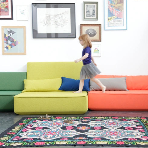 3 Sitzer Sofa in Grün, Gelb und Orange, kombiniert mit dekorativen Bildern und modernem Teppich.