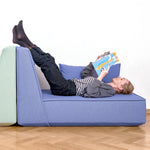 Person liegt bequem auf einem Cubit Sofa und liest ein Magazin – die Szene betont den hohen Sitz- und Liegekomfort der modularen Polstermöbel