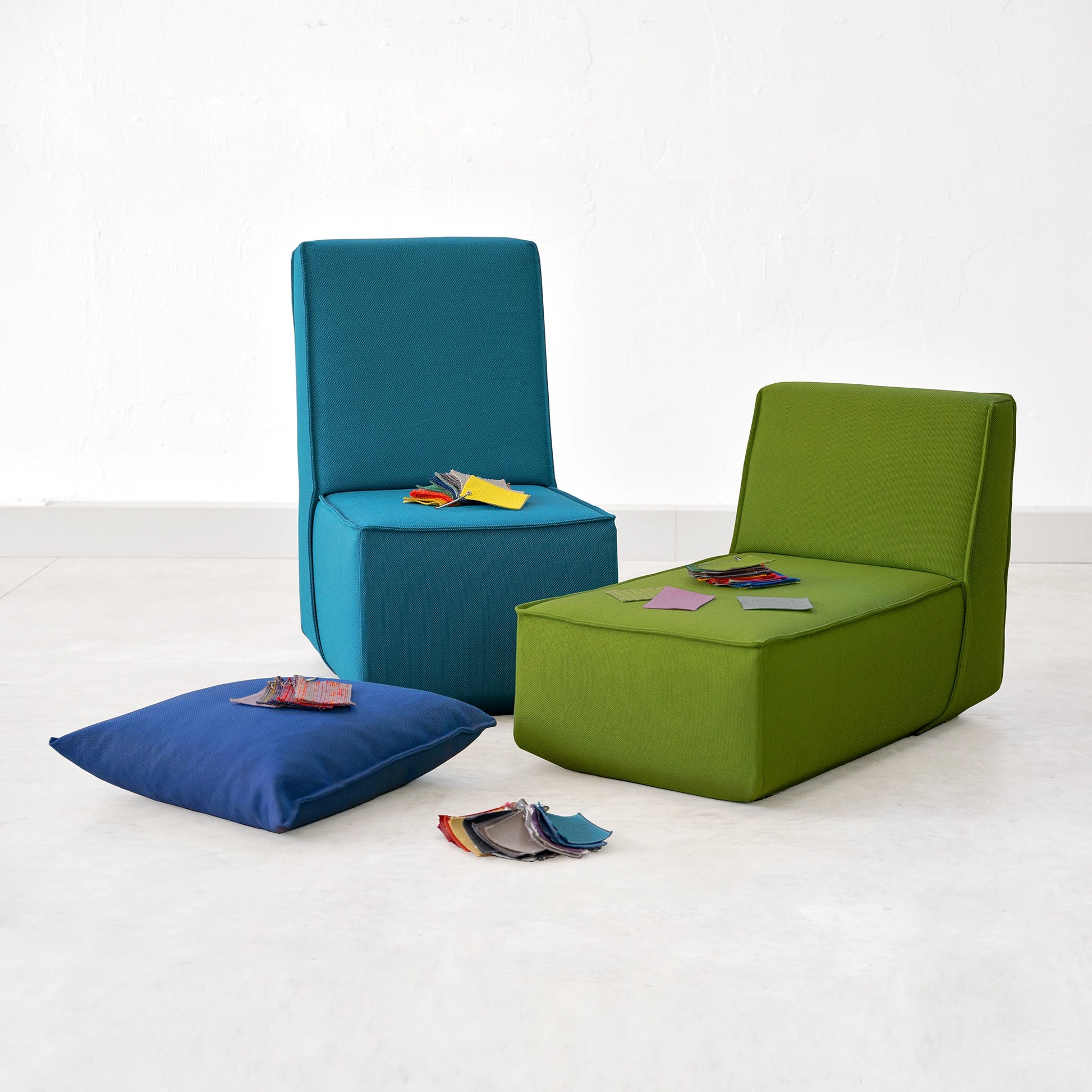 Zwei Sofaelemente in Blau und Grün, präsentiert mit Stoffmustern für Kunden zur Ansicht