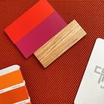 Farb- und Materialmuster auf orangefarbenem Textilstoff: Lackmuster in Rot- und Beerentönen, Holzdekor und Farbfächer