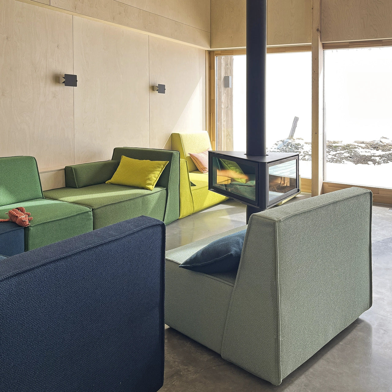 Comfortably arranged Cubit sofas in various shades of green around a central fireplace in a light-flooded loft in Méaudre