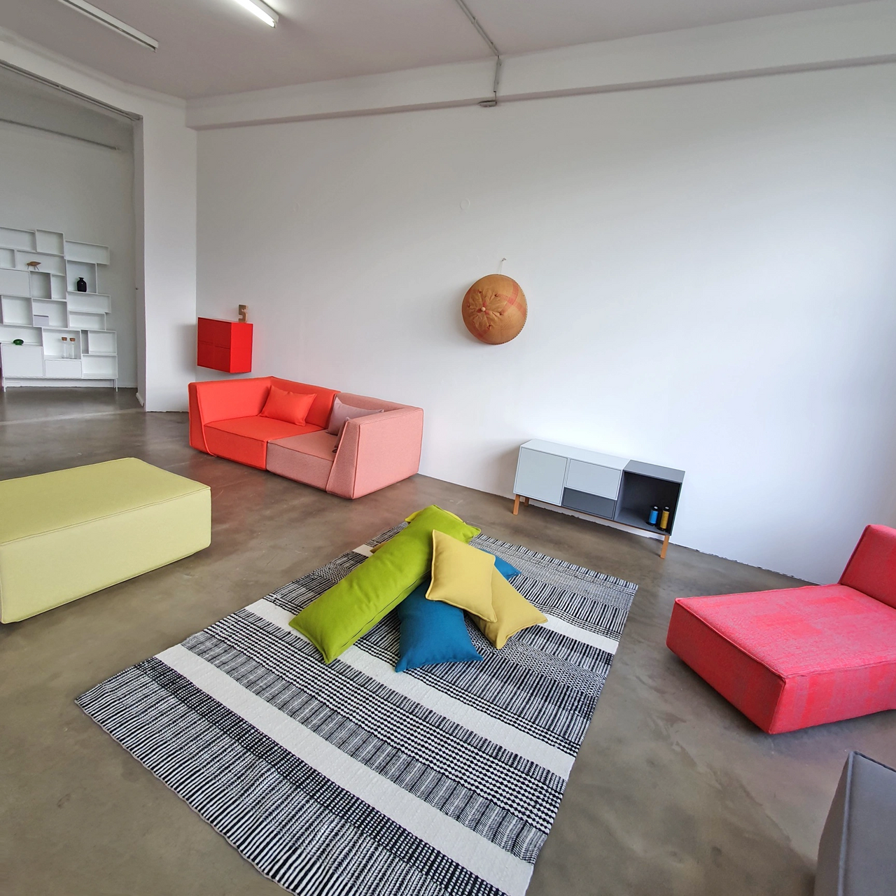 View of the Cubit showroom in Berlin with modular sofas in pink, red and green, minimalist shelves and a sideboard on oak legs in front of a white wall on a concrete floor