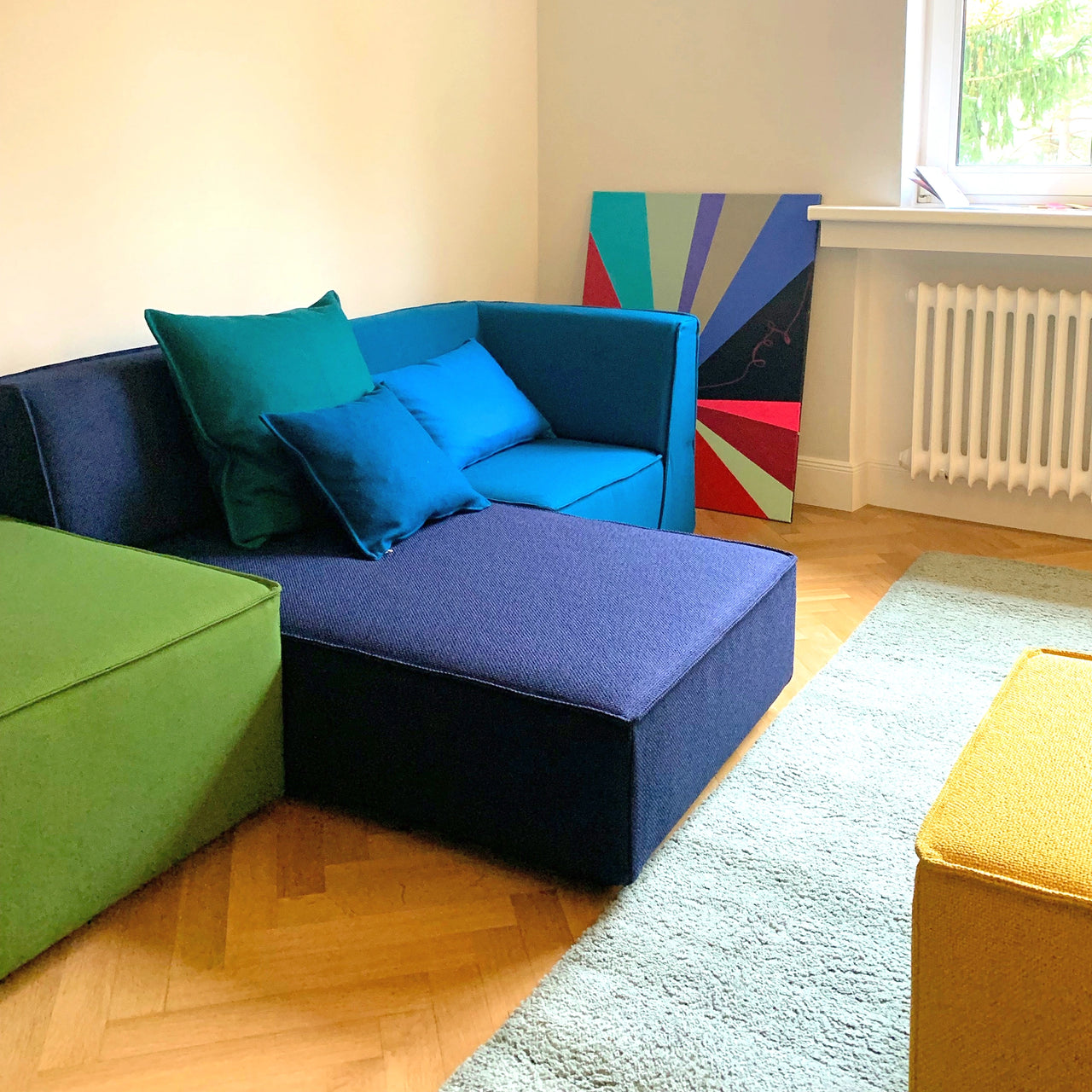 Color-coordinated Cubit sofa modules in green, blue and yellow with cushions in the Munich showroom, on parquet flooring with carpet
