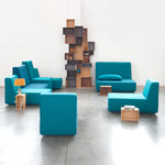 Modular sofa in turquoise blue, flexibly arranged, combined with high shelving wall made of wooden modules in the room