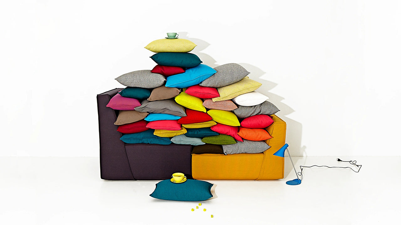 High stack of pillows in numerous colors on two Cubit Sofa modules arranged – symbolizes the variety of sofa cushions for individual design options