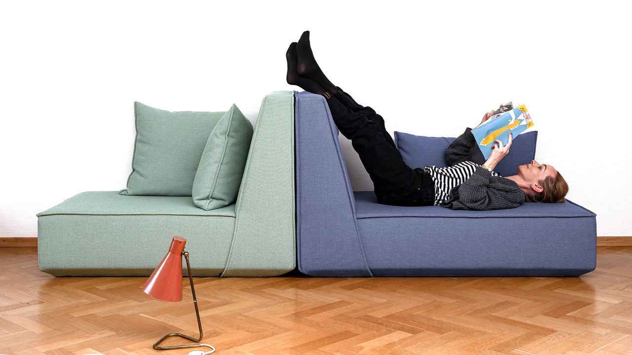 A person lies relaxed on a Cubit Sofa module and reads a magazine – the picture shows the comfortable upholstery and ergonomics of the modular sofas