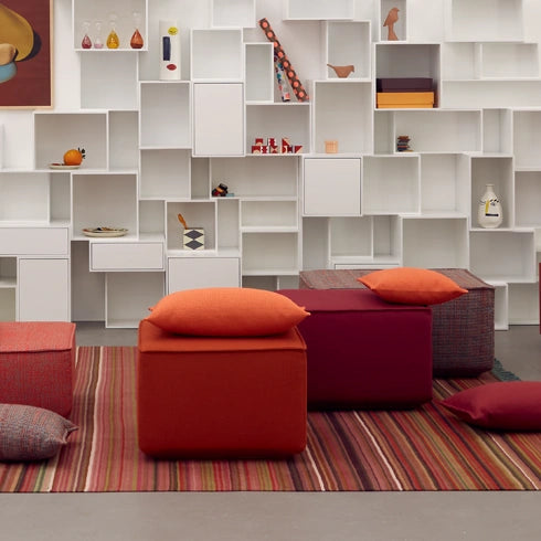 Poufs in red and orange on a striped carpet, combined with a modern shelving unit.