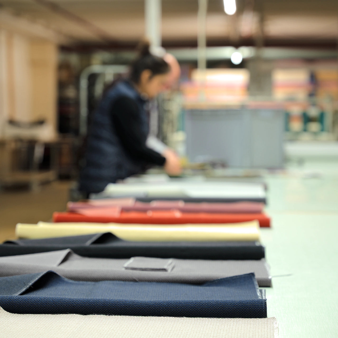 Cutting fabric lengths in the internal sewing room, with sorted fabric samples in the foreground