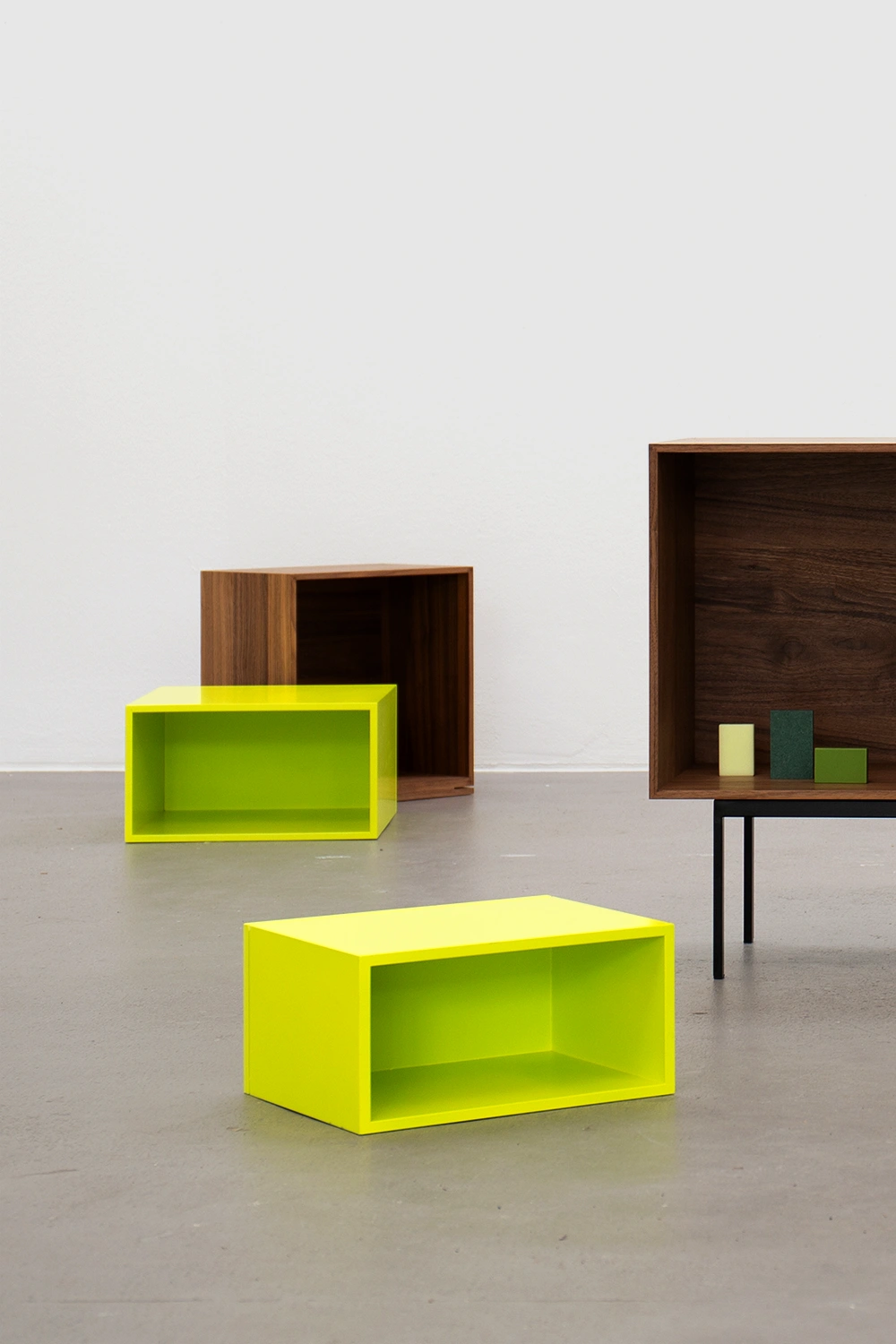 Three modular Cubit shelf boxes, two in light green and one in walnut veneer, arranged freely on the floor, another on a black metal frame