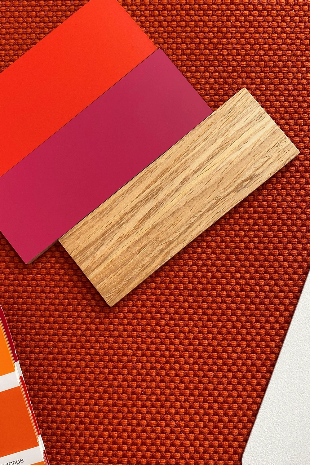 Color and material samples on a textured fabric background, consisting of two lacquer samples and a wood veneer strip