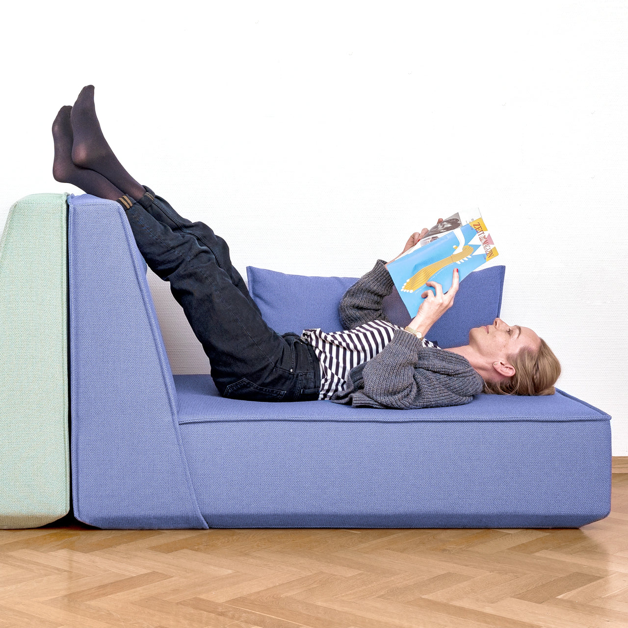 Persona comodamente sdraiata su un divano Cubit e intenta a leggere una rivista: la scena sottolinea l'elevato comfort di seduta e di reclinazione dei mobili imbottiti modulari.