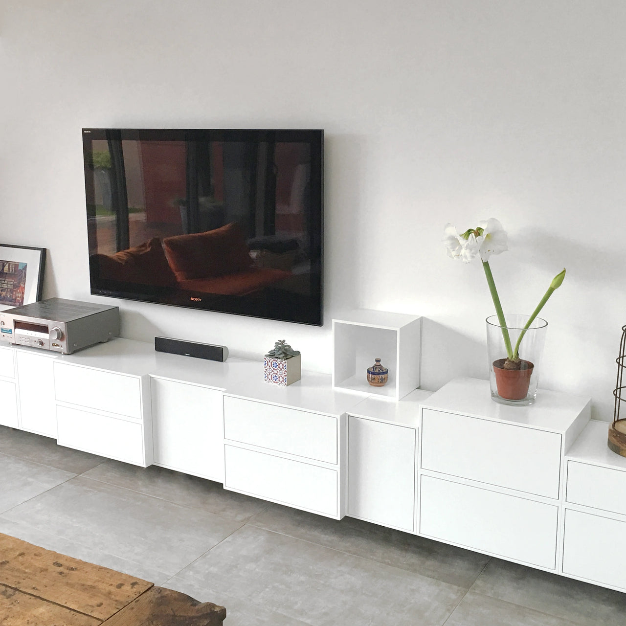 Moderno scaffale hi-fi bianco con cassetti e moduli aperti, decorato con piante e ceramiche, sotto un televisore a parete