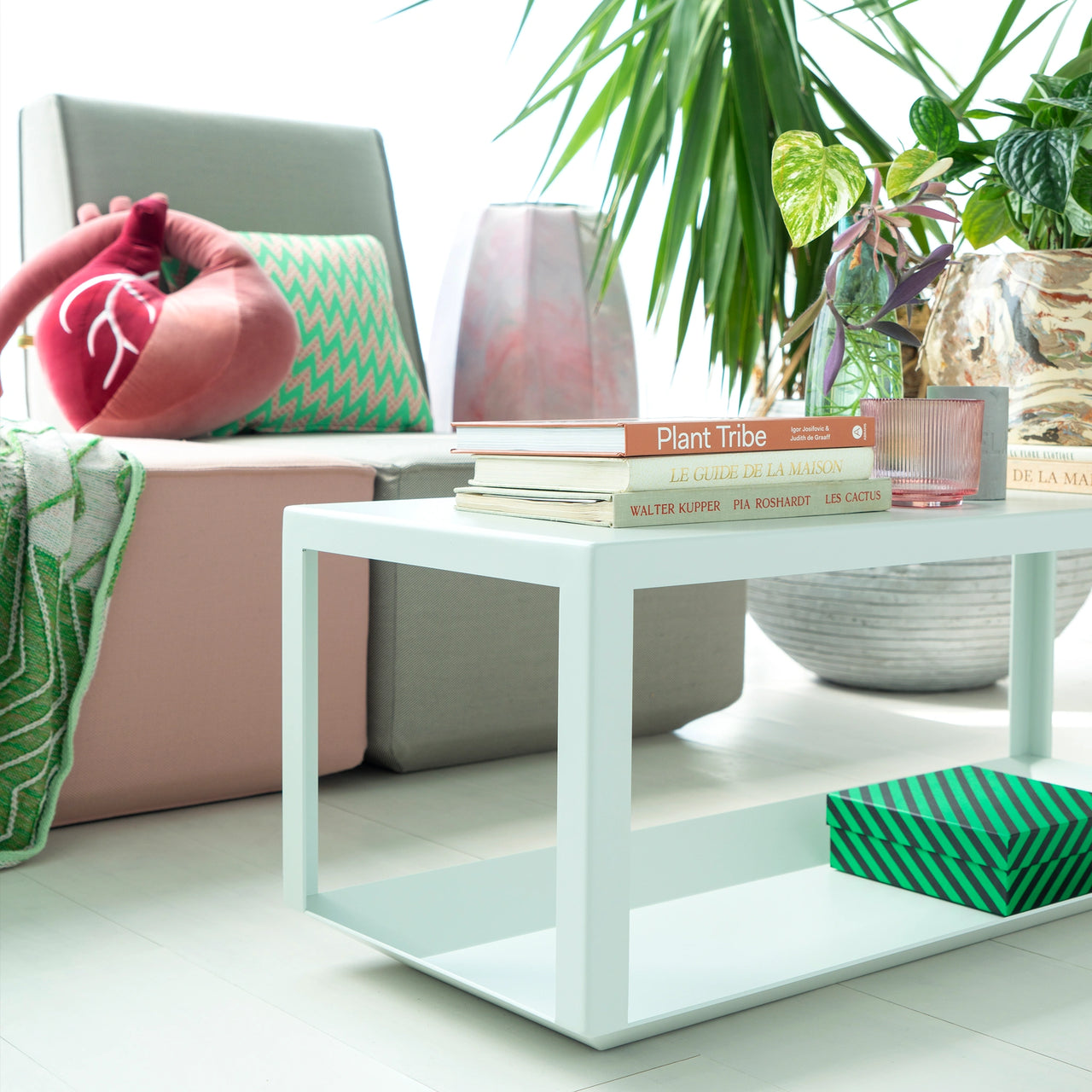 Tavolino semplice con libri e decorazioni, abbinato a sedute modulari e piante in una stanza dall'arredamento luminoso