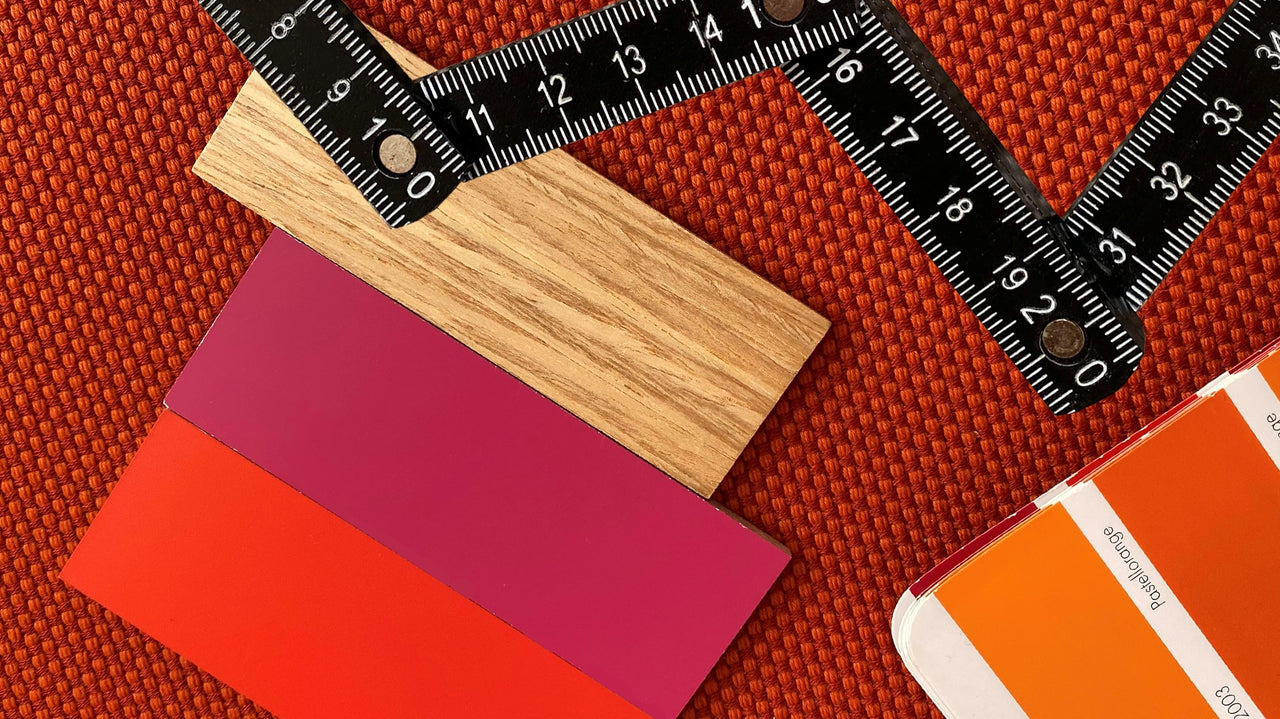 Motivo cromatico e materico con toni di legno, rosso e magenta e un regolo pieghevole nero su un tessuto arancione con trama a rilievo